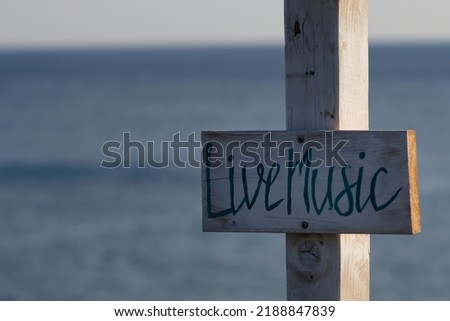 View of wooden signs for Take away and Live music and the sea in the background on the beach of Mylopotas in Ios Greece