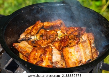 Close-up of fried pieces of pork ribs in a black cast-iron cauldron. Food in nature. Small depth of field.
