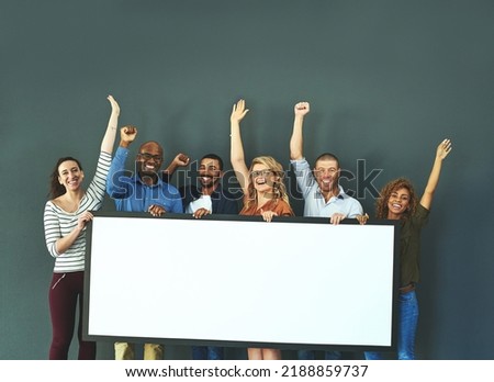 Excited business people showing a blank sign, promoting a product and giving a message on a board while standing together in an office at work. Portrait of happy colleagues holding an empty poster