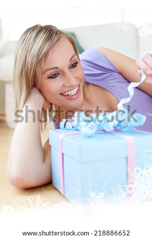 Composite image of a Cheerful blond woman holding a present lying on the floor against frost frame