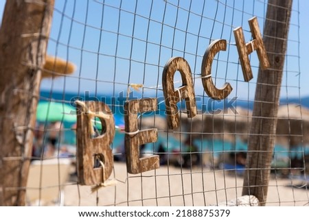 Beach sign. Wooden letters hanging. With sea and beach in background
