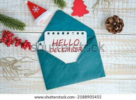 Hello December text on paper peeking out of a green envelope with new year decorations on a wooden table. Royalty-Free Stock Photo #2188905455
