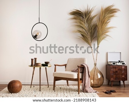 Interior design of aesthetic and minimalist living room with boucle armchair, wooden coffee table, pedant lamp, beautiful leafs in vase, decoration and personal accessories. Copy space. Home decor. Royalty-Free Stock Photo #2188908143