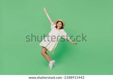 Full body young smiling woman she 20s wears white dress hat stand on toes leaning back with outstretched hands dance isolated on plain pastel light green background studio . People lifestyle concept