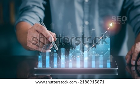 A marketer holds a pen pointing to a graph and shows SEO concepts, optimization analysis tools, search engine rankings, social media sites based on results analysis data. Royalty-Free Stock Photo #2188915871