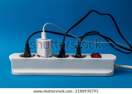 Multi-plug power strip with many connected devices on blue background. Concept of energy abuse. Waste and squandering of electricity Royalty-Free Stock Photo #2188930795