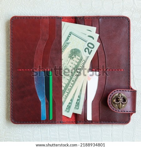 Open red leather clutch with money and credit cards on light leather background.