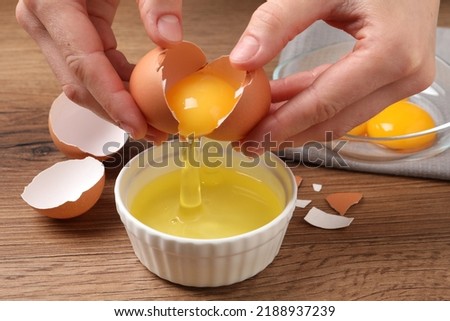 Woman separating egg yolk from white over bowl at wooden table, closeup Royalty-Free Stock Photo #2188937239