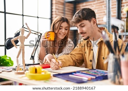 Mand and woman artist couple drinking coffee drawing on notebook at art studio