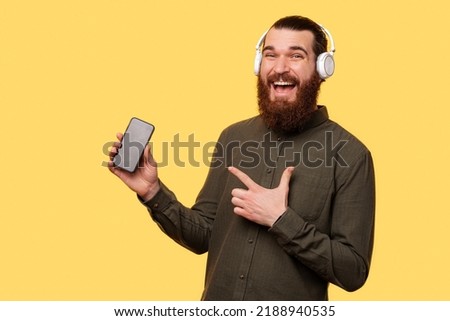 A picture of a man with headphones pointing to his new phone