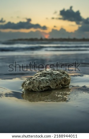A rock on water in a beach in acre with beautiful reflection, clouds, orange sky, focus on rock, blur, shallow depth of field