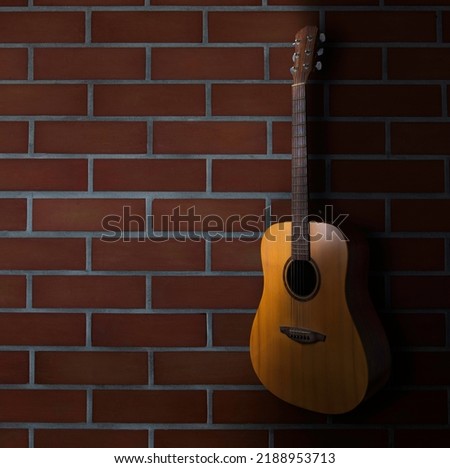 brown acoustic guitar stand in front of brick wall background. Guitar body part front made with top solid, side and back mahogany wood.
