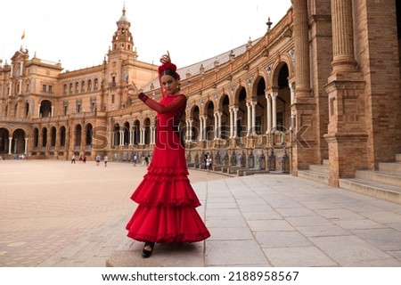 Beautiful teenage woman dancing flamenco in a square in Seville, Spain. She wears a red dress with ruffles and dances flamenco with a lot of art. Flamenco cultural heritage of humanity. Royalty-Free Stock Photo #2188958567