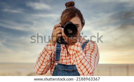 Panoramic front woman portrait of a professional travel blogger looking through the viewfinder of her camera. Front view of a woman photographer shooting to create  content. Travel woman photography