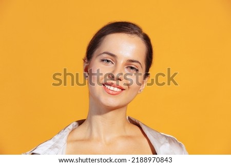 Portrait of young beautiful woman smiling at camera, posing isolated over yellow studio background. Looks delightful. Concept of beauty, lifestyle, youth, emotions, facial expression, ad. Close-up