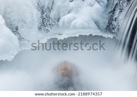 Winter landscape of a cascade on Orangeville Creek captured with motion blur and framed by ice, Michigan, USA