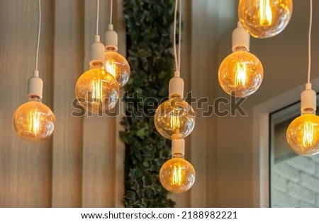 Vintage tungsten filament multiple lamps hanging from the ceiling on a white wires as an interior design concept. Energy and design concept Royalty-Free Stock Photo #2188982221