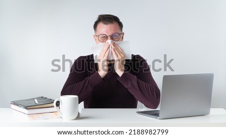 A man sneezes or blows his nose at the workplace in the office. High quality photo