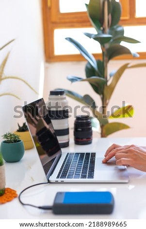 Photographer's workplace, laptop and camera lenses on a white table, photographer concept with digital camera, external harddisk, hands on keyboard close up