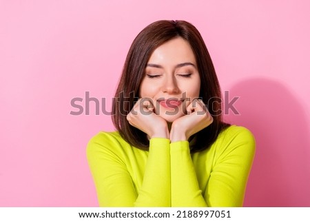 Photo of cute dreamy lady wear yellow top empty space arms cheeks chin closed eyes isolated pink color background