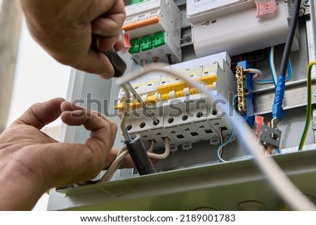Fastening circuit breakers to DIN rail of consumer unit of electrical panel. Mounting fuse box for distribution board. Royalty-Free Stock Photo #2189001783
