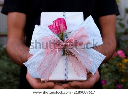 White gift with blue and pink ribbons and a bud rose in the middle on the street in male hands