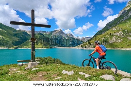 active senior woman, riding her electric mountain bike at Spuller Lake in the Arlberg area near the famous village of Lech, Tirol, Austrian Alps Royalty-Free Stock Photo #2189012975