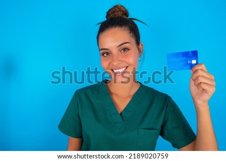 Photo of happy cheerful smiling positive Caucasian doctor woman with medical uniform over blue background recommend credit card