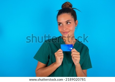 Photo of cheerful Caucasian doctor woman with medical uniform over blue background hold debit card look empty space
