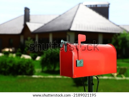 Red letter box and blurred view of modern house with beautiful garden on sunny day