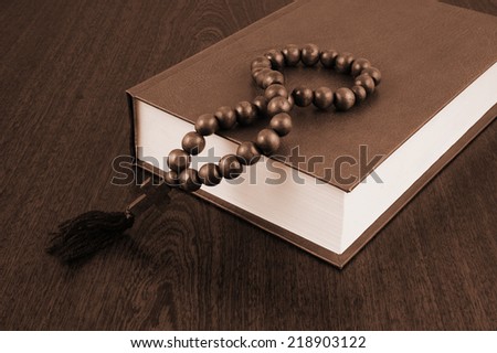 The holy bible and rosary beads on wooden background 