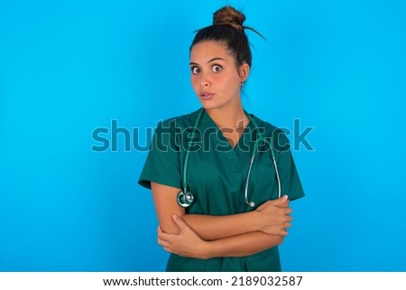 beautiful doctor woman wearing medical uniform over blue background shaking and freezing for winter cold with sad and shock expression on face.