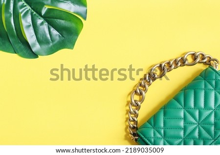 Stylish women's fashionable green quilted handbag with a large gold chain and a large carved green leaf on the sides on a yellow background with copy space in the center, close-up.Fashion accessories 
