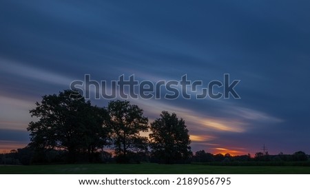 Übersetzen
Orange, blue landscape shot with rising sun and silhouette of trees.