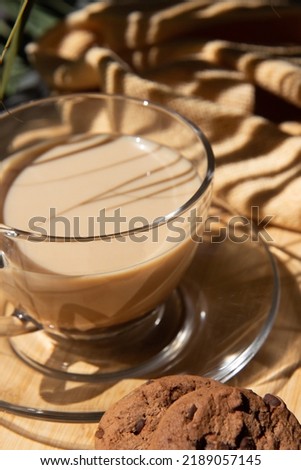 Glass cup with fragrant cappuccino coffee and chocolate chip cookies on a summer veranda against the backdrop of palm trees
