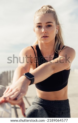 Portrait of confident young woman listening music and stretching hands while exercising against sky on sunny day