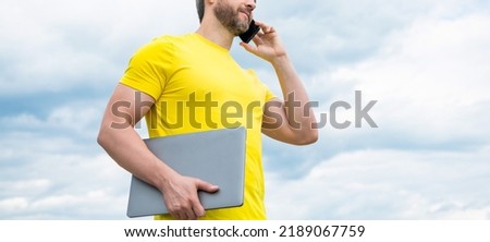 cropped view of man with laptop talking on smartphone on sky background
