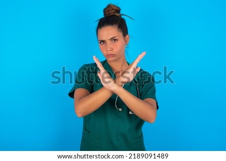 beautiful doctor woman wearing medical uniform over blue background Rejection expression crossing arms doing negative sign, angry face