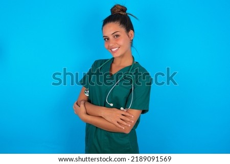 beautiful doctor woman wearing medical uniform over blue background happy face smiling with crossed arms looking at the camera. Positive person.