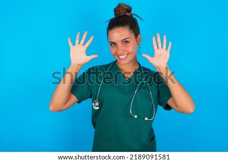 beautiful doctor woman wearing medical uniform over blue background showing and pointing up with fingers number ten while smiling confident and happy.