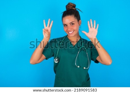 beautiful doctor woman wearing medical uniform over blue background showing and pointing up with fingers number eight while smiling confident and happy.