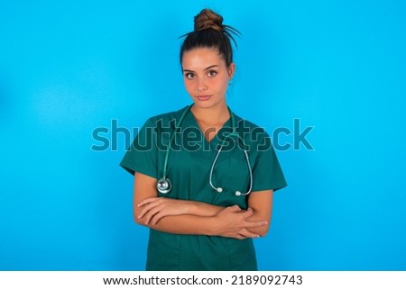 Serious pensive beautiful doctor woman wearing medical uniform over blue background feel like cool confident entrepreneur cross hands.