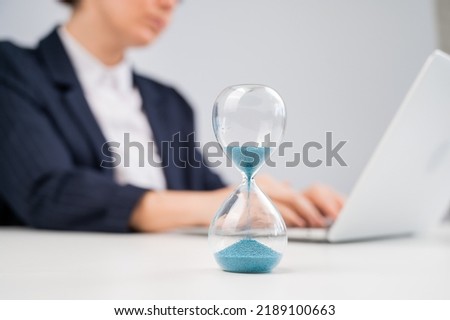 Business woman keeps track of time on an hourglass while working. Royalty-Free Stock Photo #2189100663