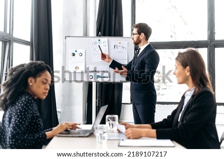 Influential Caucasian attractive male ceo, holding group brainstorm, discussing ideas for a new business project, makes a business plan presentation to his female partners. Teamwork, collaboration Royalty-Free Stock Photo #2189107217