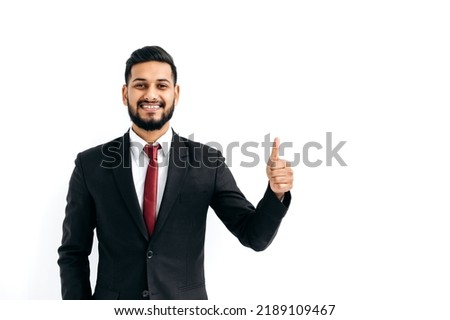 Successful handsome confident indian or arabian businessman in a black business suit, standing over isolated white background, showing thumb up, agree sign, looking at camera, smiling happily Royalty-Free Stock Photo #2189109467