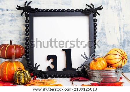 Halloween holiday concept with empty black frame, spiders and pumpkins on a light table against a light wall. copy space,