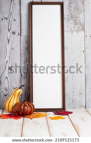 Mock up wood frame with autumn leaves and pumpkins on a light shelf. fall concept. Portrait frame against a white wall. copy space