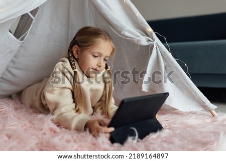 Caucasian kid studying online at home and using tablet. Distance or remote learning for child. Pretty stylish schoolgirl studying homework during coronavirus covid-19 quarantine and social