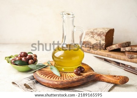 Wooden board with decanter of fresh olive oil on light background