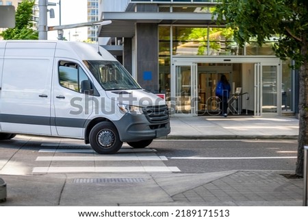 Industrial standard for local deliveries and short haul freights or small business services compact white mini van turning to building parking garage entrance for goods delivery and unloads Royalty-Free Stock Photo #2189171513